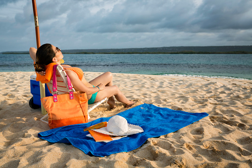 Hispanic Young woman relaxing and resting under beach umbrella on a tropical white sand island beach in the Caribbean sea