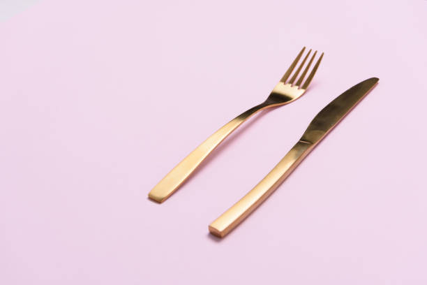 istock Golden fork and knife on light pink background with negative space. 994710370