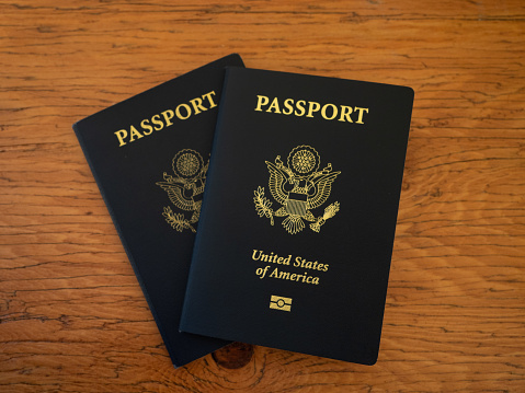 Two navy blue US Passports on a wooden table top and photographed from above.