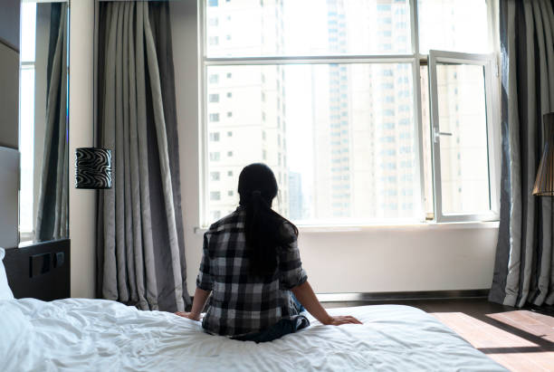 istock girl sitting on bed, looking out through window 994775024