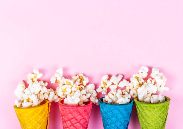 istock Delicate pink background and sweets. Sweet popcorn and colored waffles. scattered popcorn 994786976