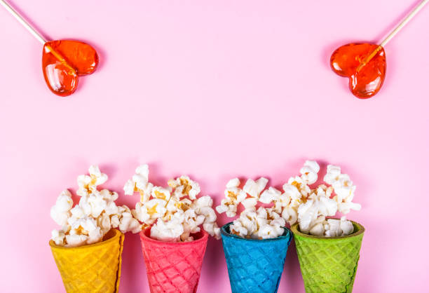 istock Pink background and sweets. Sparse popcorn and lollipops. Copy space. Popcorn in a waffle cone 994790564