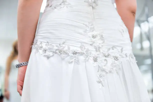 Closeup back of young woman trying on zipper zipped wedding dress in boutique discount store, fitness watch