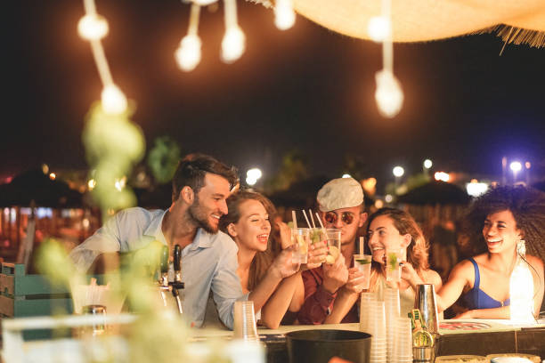 amis heureux acclamant et boire des cocktails à la fête de plage plein air - millennials jeunes gens s’amuser au foyer d’accueil de nuit - concept de mode de vie et la vie nocturne des jeunes - week-end été les gars gauche - entertainment photos et images de collection