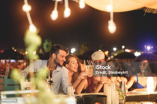 Happy Friends Cheering And Drinking Cocktails At Beach Party Outdoor Young Millennials People Having Fun At Weekend Summer Night Youth Lifestyle And Nightlife Concept Main Focus On Left Guys Stock Photo - Download Image Now
