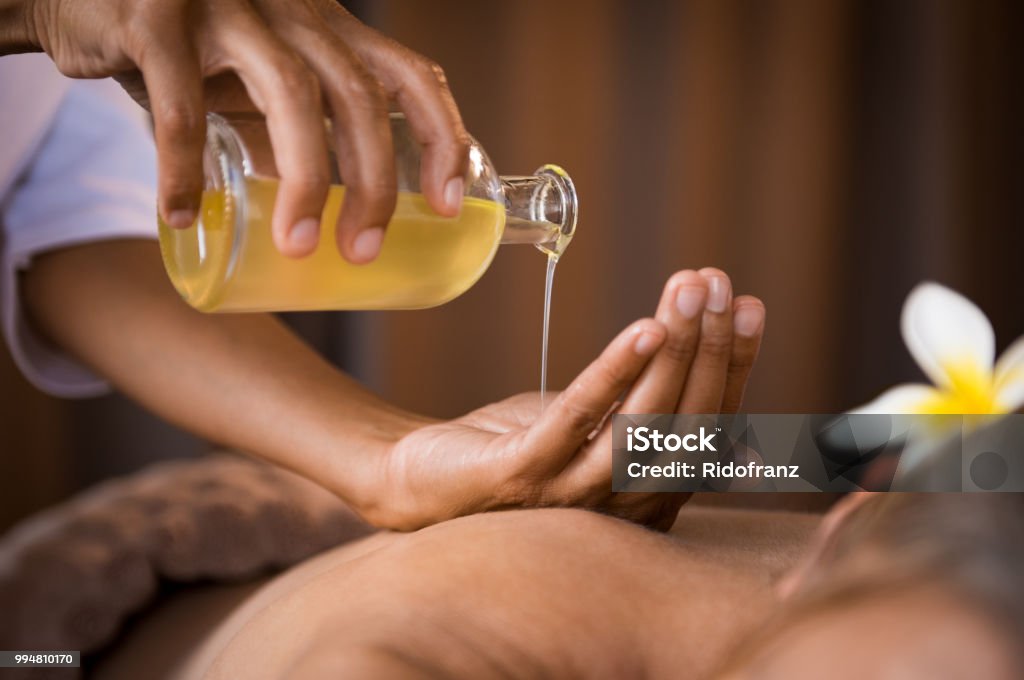 Therapist pouring massage oil at spa Closeup of masseur hands pouring aroma oil on woman back. Masseuse prepare to do oriental spa procedure for relaxing treatment. Therapist doing aromatherapy oil massage on woman body. Massaging Stock Photo