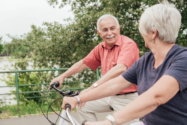 istock Senior man smiling while riding a bicycle and looking at the woman by him 994810292