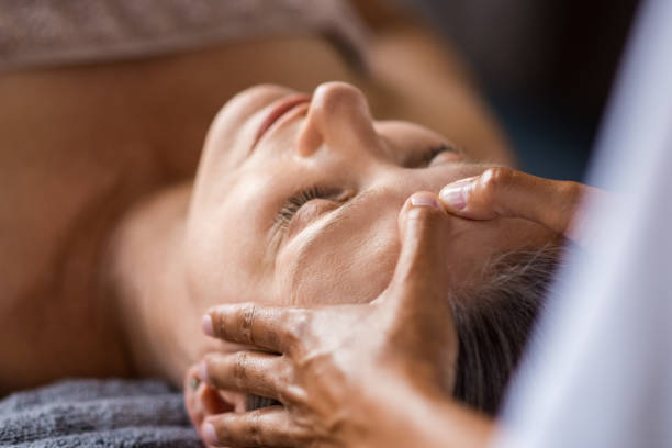 Anti-aging facial treatment Closeup face of mature woman having facial massage at spa. Senior woman lying with closed eyes at spa while a massage therapist doing anti-aging treatment. Masseur doing head massage at wellness center. relaxation lying on back women enjoyment stock pictures, royalty-free photos & images