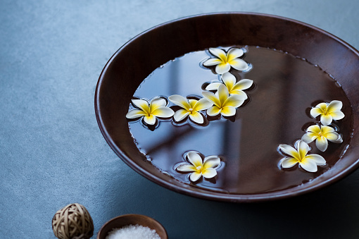 Closeup of frangipani flowers floating in bowl of water at wellness center. White flowers in wooden bowl with water for aroma therapy at spa. Spa setting for beauty treatment.