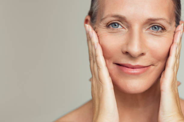 Happy mature woman aging process Portrait of beautiful senior woman touching her perfect skin and looking at camera. Closeup face of mature woman with wrinkles massaging face isolated over grey background. Aging process concept. wrinkled stock pictures, royalty-free photos & images