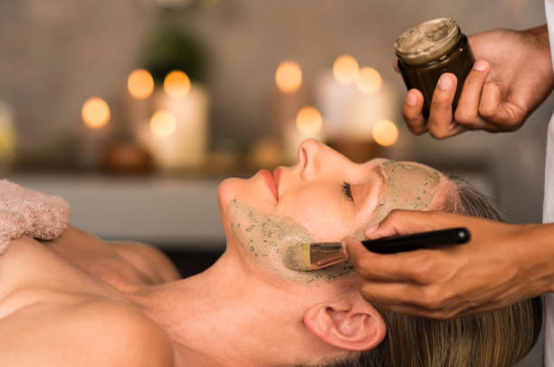 Woman with clay mask on face Senior woman relaxing while beautician getting purifying clay mask on her face. Closeup hand of masseuse applying mud from jar container on face of mature lady in spa center. Anti aging facial treatment with brush. exfoliating scrub stock pictures, royalty-free photos & images