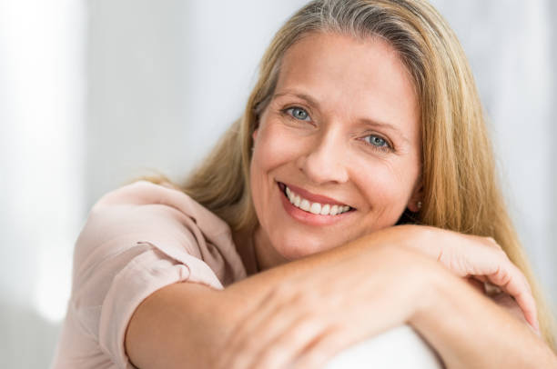 улыбающаяся зрелая женщина на диване - women smiling blond hair cheerful стоковые фото и изображения