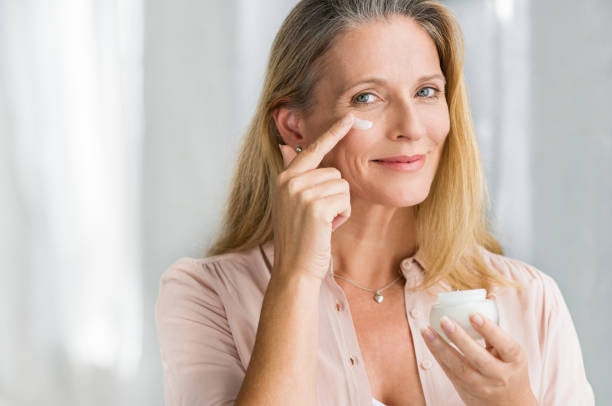 Woman applying anti aging lotion on face Smiling senior woman applying anti-aging lotion to remove dark circles under eyes. Happy mature woman using cosmetic cream to hide wrinkles below eyes. Lady using day moisturizer to counteract the aging of the skin. antiaging stock pictures, royalty-free photos & images