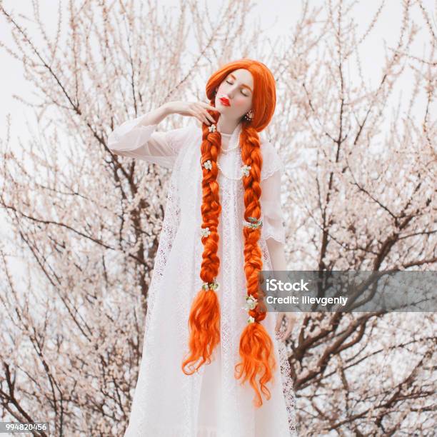 Young Beautiful Unusual Redhead Girl With Curly Hair Braided In Plait On A Spring Background A Woman With Pale Skin And Very Long Red Plait In A Preraphaelite Dress Stock Photo - Download Image Now