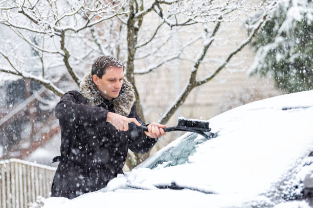 istock Young man cleaning car windshield from snow, ice with brush and scraper tool during snowfall during winter snowing snowflakes falling 994826696