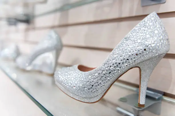 Closeup of many shining wedding, high heels style shoes on shelf embellished with crystals, pearls, embellishments on retail display in store, shop, shopping mall