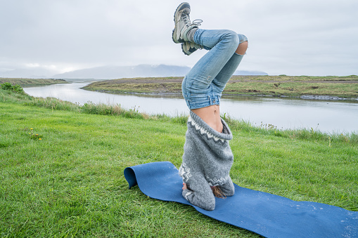 Young woman exercising yoga headstand pose in pure nature, Iceland. People travel healthy lifestyle and yoga concept