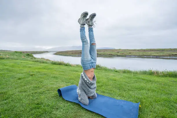 Young woman exercising yoga headstand pose in pure nature, Iceland. People travel healthy lifestyle and yoga concept
