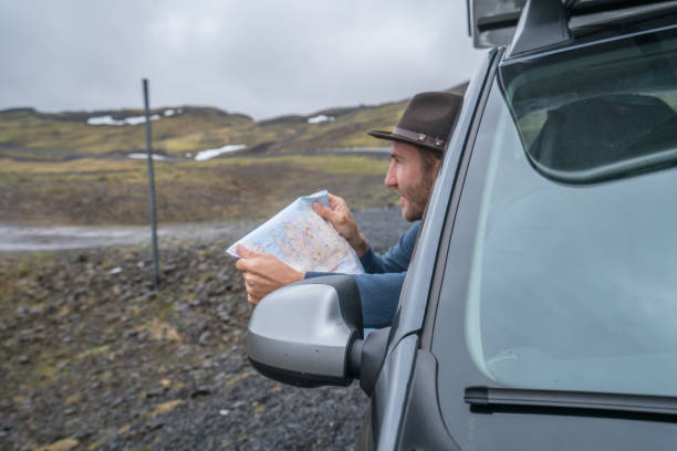 istock Young man in car looking at map, road trip concept vacations 994838392
