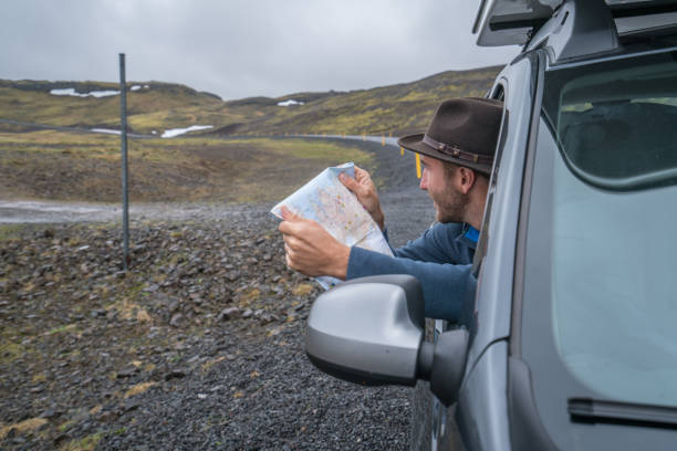 istock Young man in car looking at map, road trip concept vacations 994838404