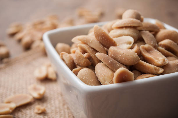 salted peanuts in a porcelain bowl on wooden background stock photo