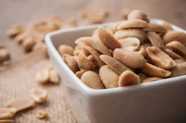 closeup of salted peanuts in a porcelain bowl on wooden background