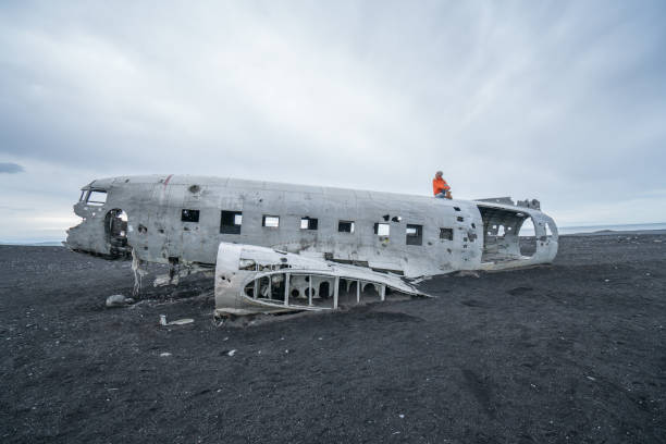 istock Young woman stands on airplane crashed on black sand beach looking around her contemplating surroundings 994850002
