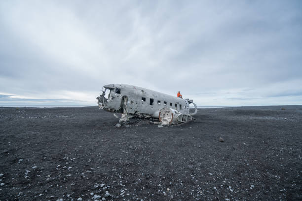 istock Young woman stands on airplane crashed on black sand beach looking around her contemplating surroundings 994850022