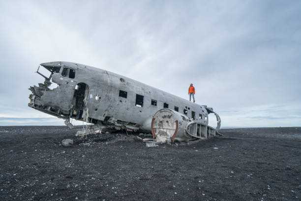 istock Young woman stands on airplane crashed on black sand beach looking around her contemplating surroundings 994850046