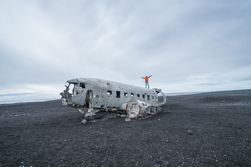 Young woman stands arms outstretched on airplane crashed on black sand beach looking around her contemplating surroundings
Famous place to visit in Iceland and pose with the wreck