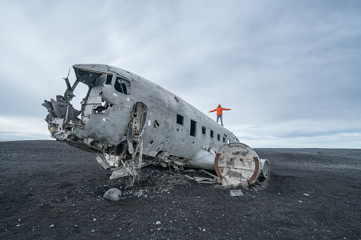Young woman stands arms outstretched on airplane crashed on black sand beach looking around her contemplating surroundings
Famous place to visit in Iceland and pose with the wreck