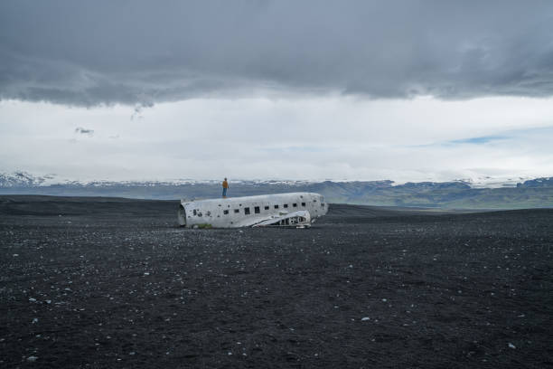 istock Young man stands on airplane crashed on black sand beach looking around her contemplating surroundings 994850456