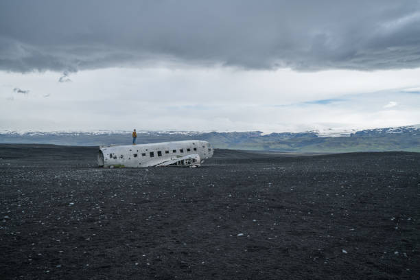 istock Young man stands on airplane crashed on black sand beach looking around her contemplating surroundings 994850460