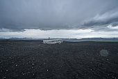 Young man stands on airplane crashed on black sand beach looking around her contemplating surroundings