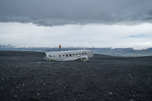 istock Young man stands on airplane crashed on black sand beach looking around her contemplating surroundings 994850480