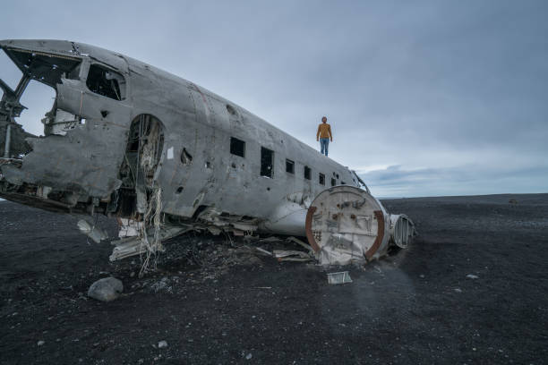 istock Young man stands on airplane crashed on black sand beach looking around her contemplating surroundings 994850574