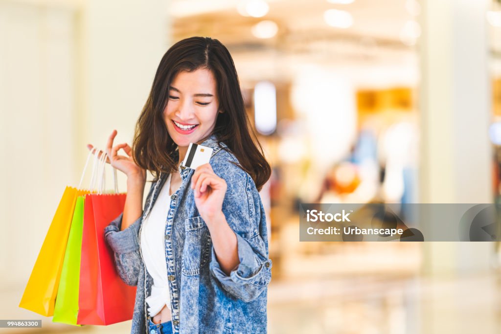 Glücklich schöne asiatische Frau Lächeln auf Kreditkarte, halten Einkaufstaschen, Textfreiraum auf Shopping-Mall-Hintergrund. Shopaholic Menschen, reiches Mädchen Taschengeld Lebensstil oder Kaufhaus Zahlung Konzept - Lizenzfrei Einkaufen Stock-Foto