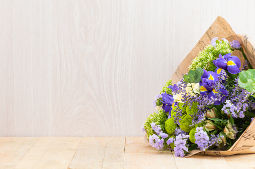 colorful bouquet of iris and other fresh flowers wrapped in paper on wooden table. Wood background with copy space for text