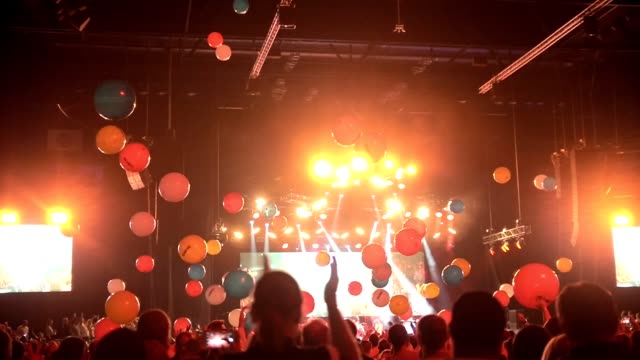 Crowd of people having fun at a concert with balloons flying around the concert hall