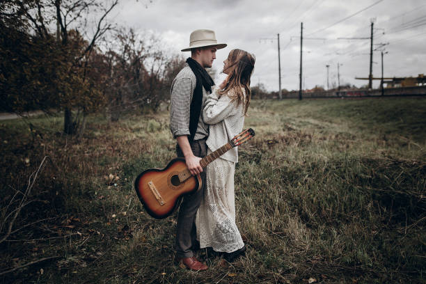 istock rustic wedding concept. boho gypsy woman and man with guitar posing in windy field. stylish hipster couple hugging. atmospheric sensual moment. fashionable look. 994884512