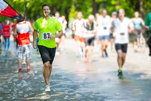 smiling man running marathon shortly after refreshment stop on sunny day in spring