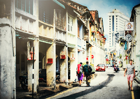 penang street with vintage buildings showing 2 backpackers walking towards the city and another Caucasian male with casual clothing walking down the street. Penang is one of the tourism city in malaysia with authentic local pre war building preserved \nimage taken 23rd july 2015 morning