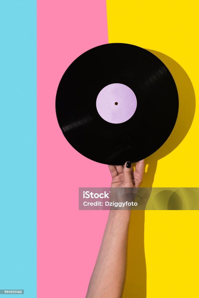 Play that music Female hand holding vinyl record over pink and blue and yellow background Record - Analog Audio Stock Photo