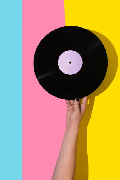 Female hand holding vinyl record over pink and blue and yellow background