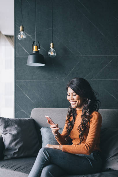 istock Woman sitting on couch, using her smartphone 994948058