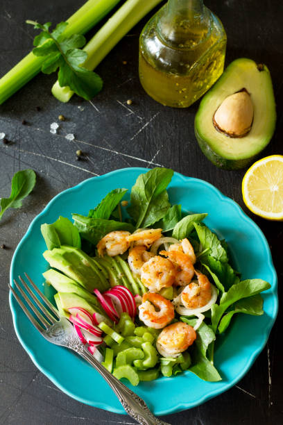 salada de vegetais saudável de camarão grelhado, rúcula, rabanete, abacate, aipo e molho vinagrete sobre um fundo escuro de ardósia. menu de dieta. - 11873 - fotografias e filmes do acervo