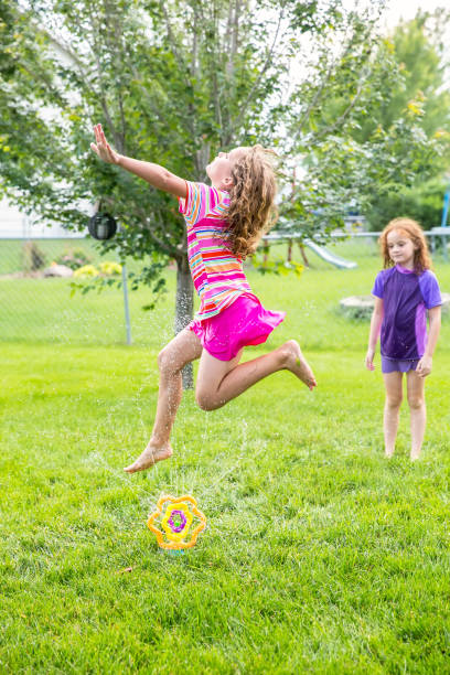 istock Two Young Girls Playing in Water Sprinkler in Back Yard 995029524