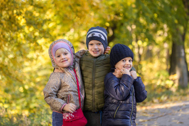 grupa szczęśliwej trójki dzieci bawiących się na świeżym powietrzu w jesiennym parku. słodkie dzieci lubią przytulać się razem na złotym tle upadku. najlepsza koncepcja frend forever i happy childhood - frend zdjęcia i obrazy z banku zdjęć