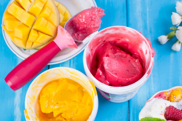istock Fruit ice cream with mango and raspberries in a bucket pack. Spoon for ice cream. Blue background and flowers. copy space. 995043234