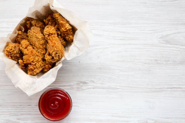istock Spicy fried chicken wings with sauce on a white wooden surface, top view. From above, flat, overhead. Copy space and text area. 995076358